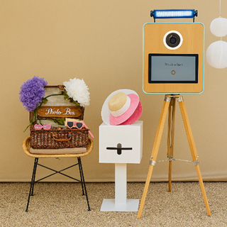 Fotobooth met accessoires in een feestelijke setting, inclusief hoeden, bloemen en een touchscreen camera op statief Fotobooth met accessoires in een feestelijke setting, inclusief hoeden, bloemen en een touchscreen camera op statief